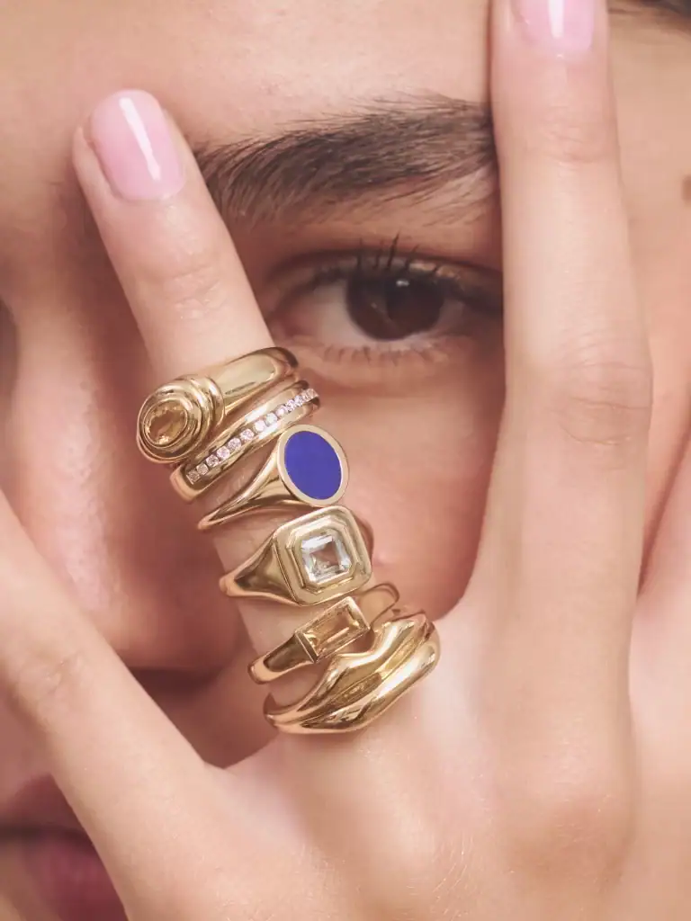 Close-up of layered gold rings with blue, clear, and embellished designs on a woman's hand.